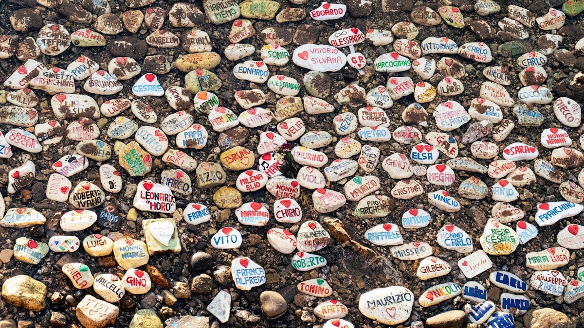 Vibrant painted stones with names on a rocky Italian beach, creating a lively artistic scene.